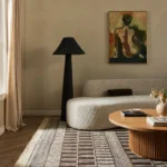 Warm neutral living room with a curved bouclé sofa, black floor lamp, striped rug and figurative painting