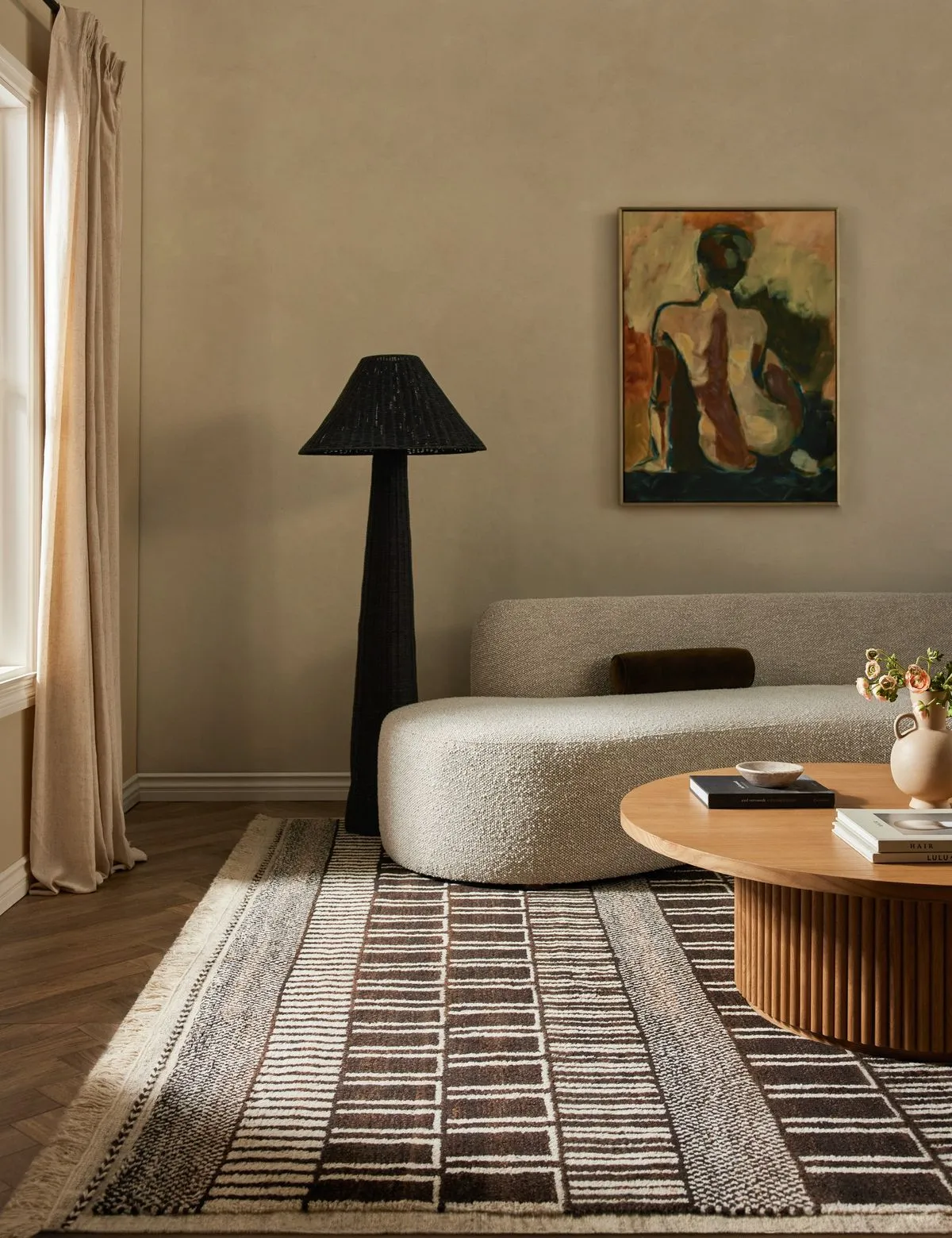 Warm neutral living room with a curved bouclé sofa, black floor lamp, striped rug and figurative painting
