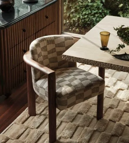 Checked bouclé dining chair with a wooden frame on a sculpted wool rug beside a stone table