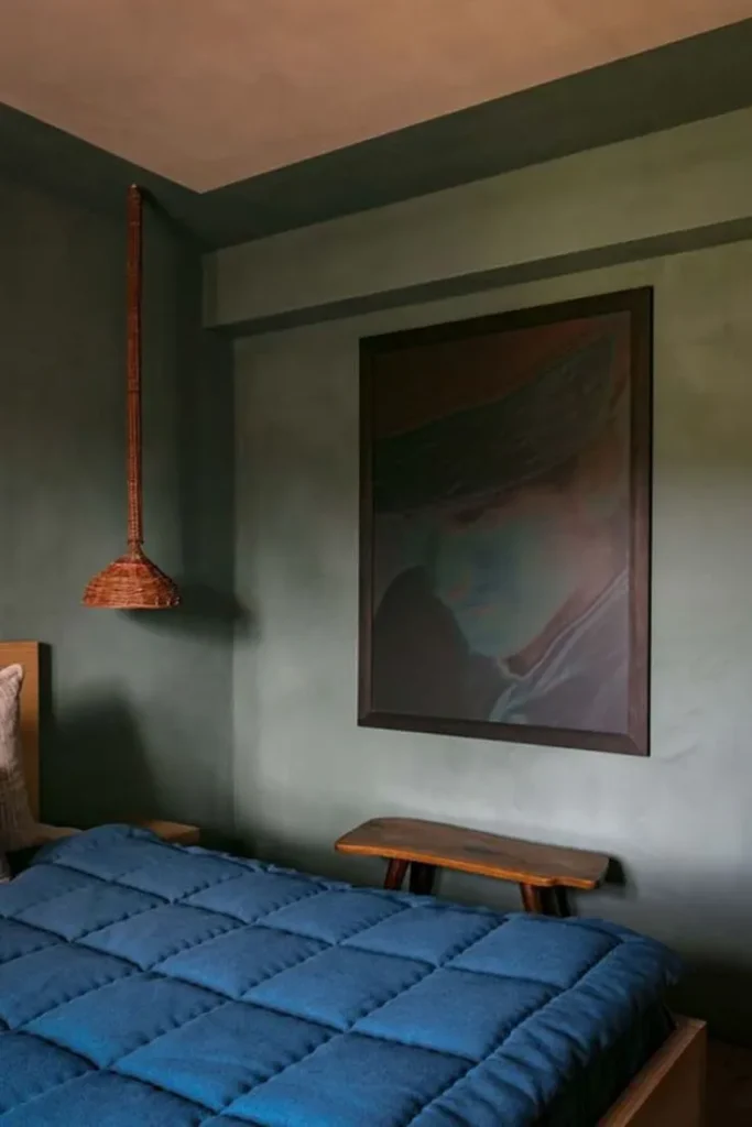 Bedroom with green limewashed walls, a large dark painting and a blue quilted bedspread