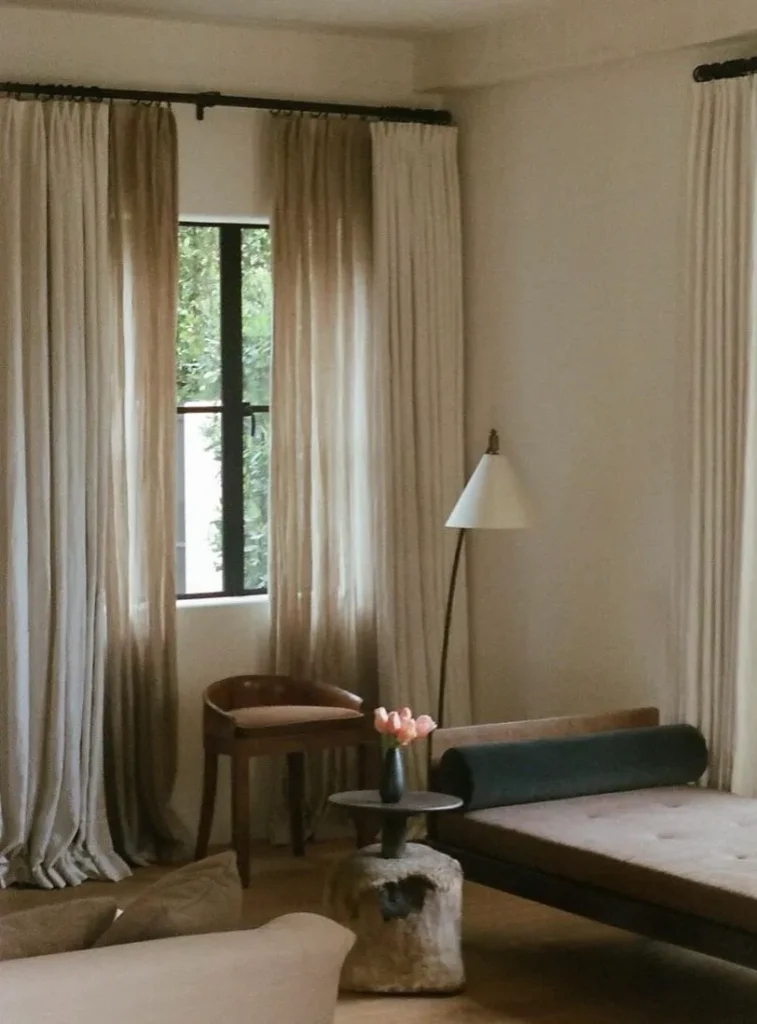 Floor-length linen curtains in a calm sitting room with a daybed and a wooden armchair