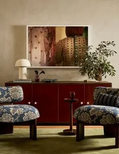 Floral upholstered lounge chairs in front of an oxblood sideboard and a large framed photograph