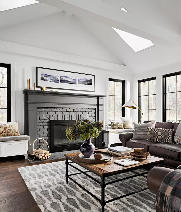 Living room with a grey brick fireplace, a vaulted ceiling with skylight and a patterned rug