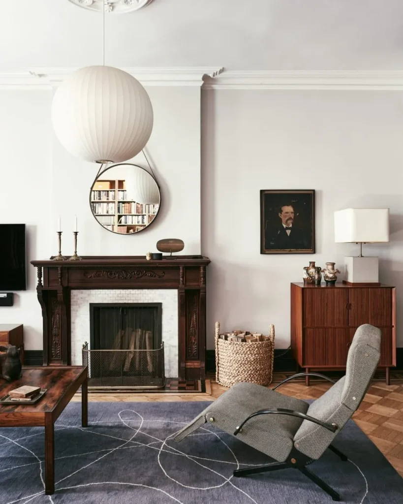 Living room with a carved wooden fireplace, globe pendant, round mirror and a grey lounge chair