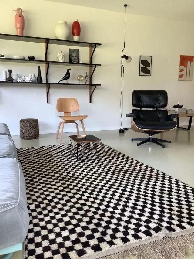 Living room with an Eames Lounge Chair, a plywood chair, wall shelves and a black-and-white checkerboard rug