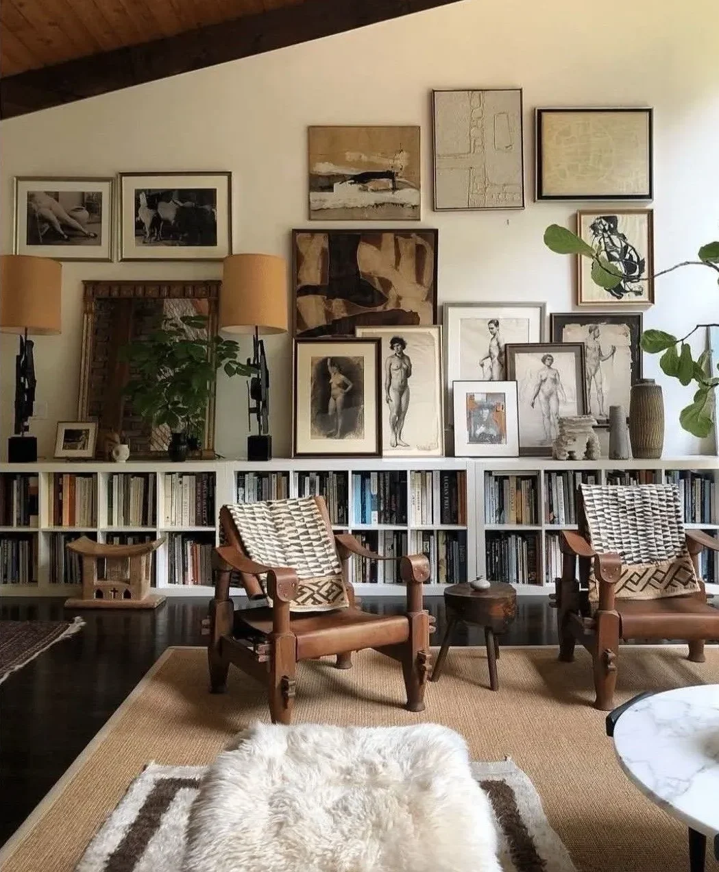 Gallery wall of photos and prints above white bookcases with two vintage wooden armchairs