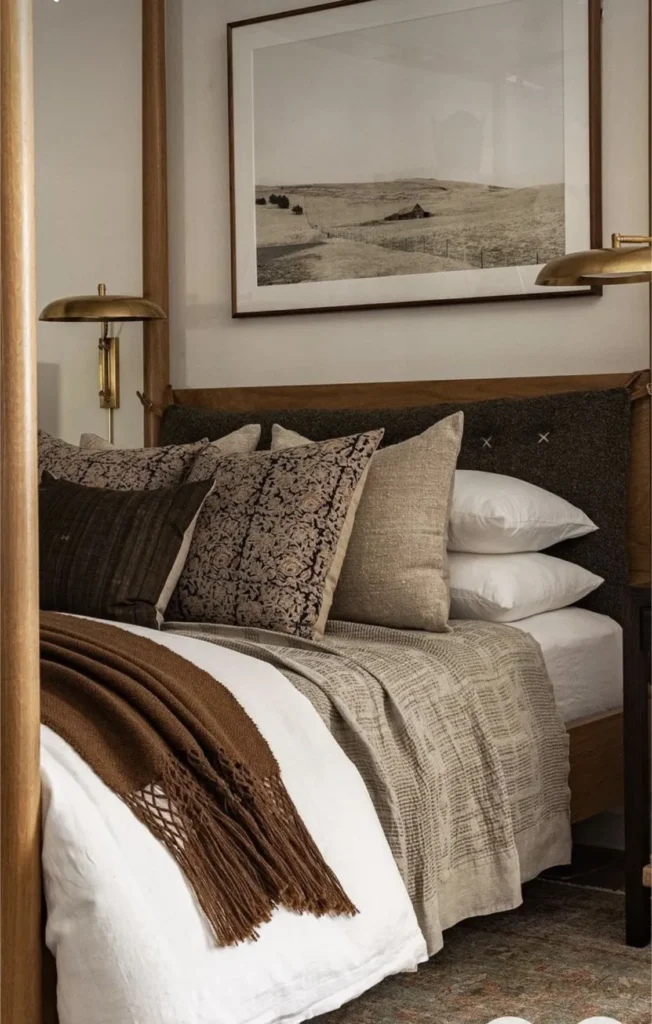 Bed layered with patterned, linen and knitted cushions and a fringed brown throw