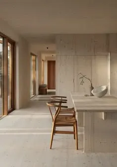 Minimal stone-coloured kitchen with a long table and a single Wishbone chair