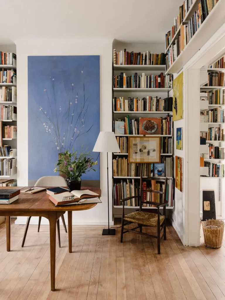 Room lined with floor-to-ceiling bookshelves, a large blue artwork and a wooden table