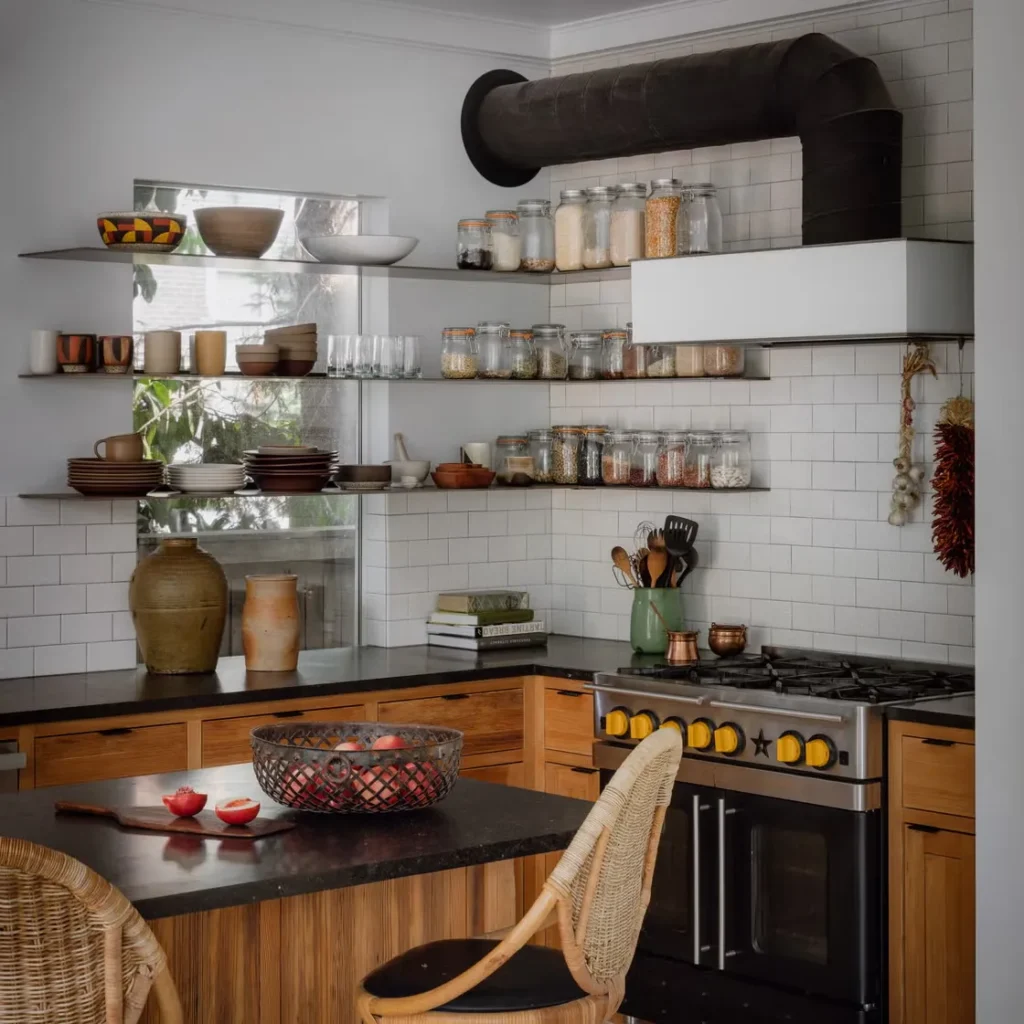 Kitchen with open glass shelves full of jars and ceramics, wooden cabinets and a black range hood