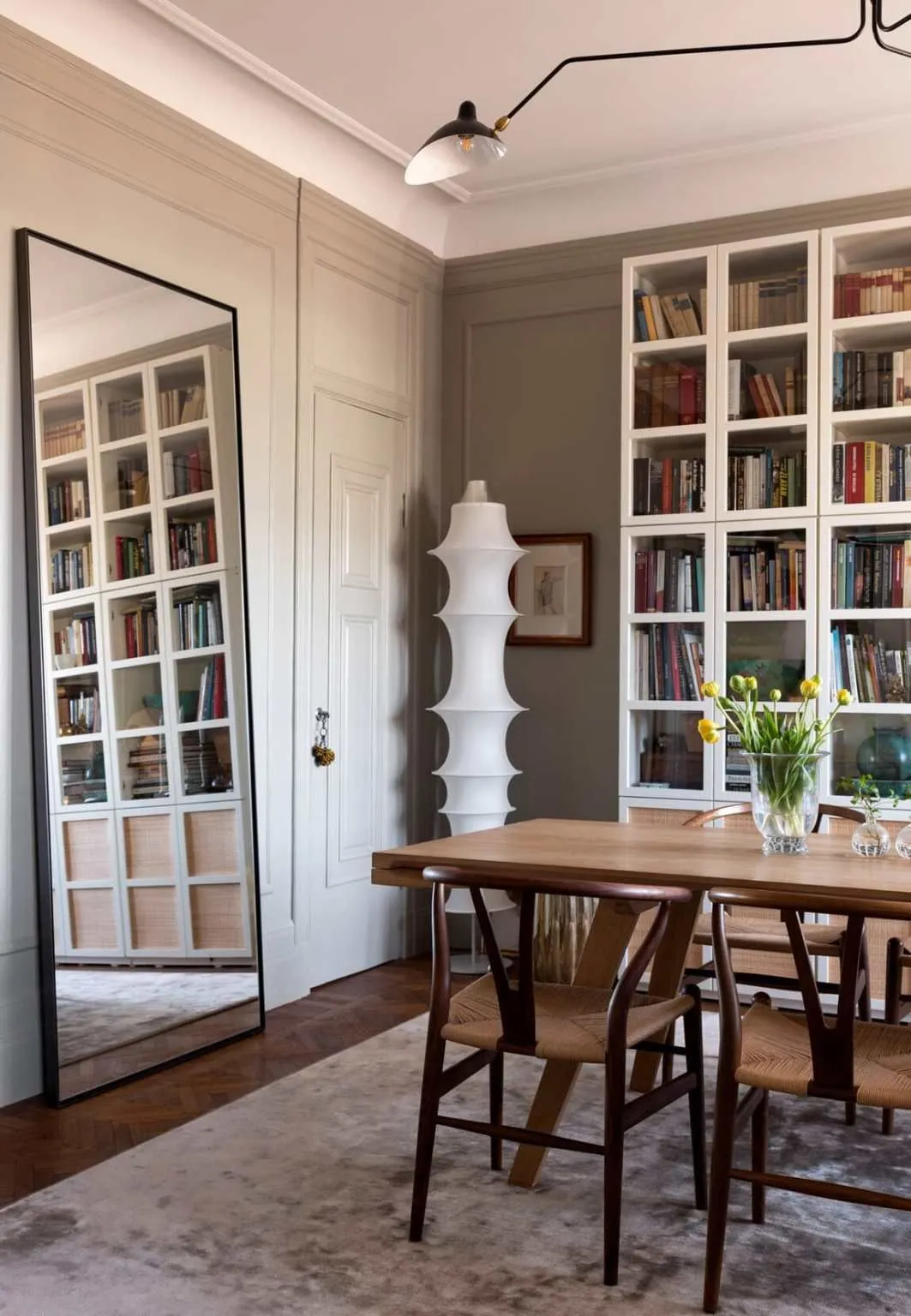 Wishbone Chairs at a wooden dining table with tall white bookcases and a floor mirror