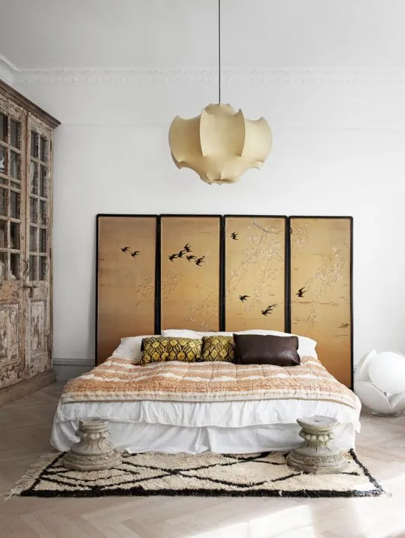 Castiglioni cocoon pendant for Flos above a bed with a gold folding screen and a Berber rug