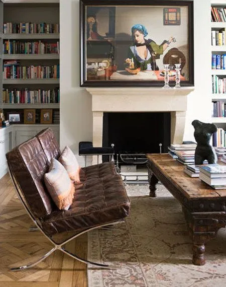 Barcelona Chair in brown leather beside a fireplace, bookshelves and a carved wooden coffee table