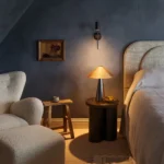 Bedroom with deep blue textured walls and matching skirting, a bouclé armchair and a brass table lamp