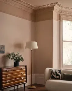 Blush-pink living room with skirting and cornice in the wall colour, a vintage chest and a floor lamp