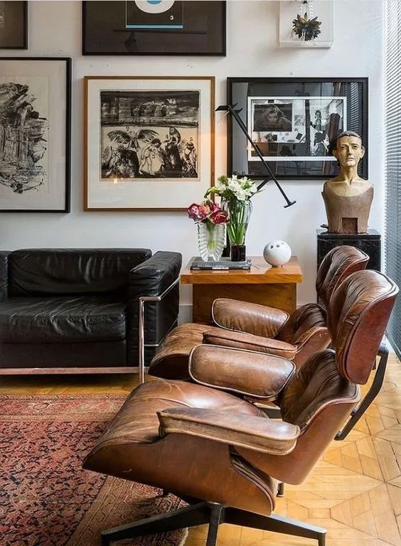 Two Eames Lounge Chairs in tan leather beside a black leather sofa and a gallery wall