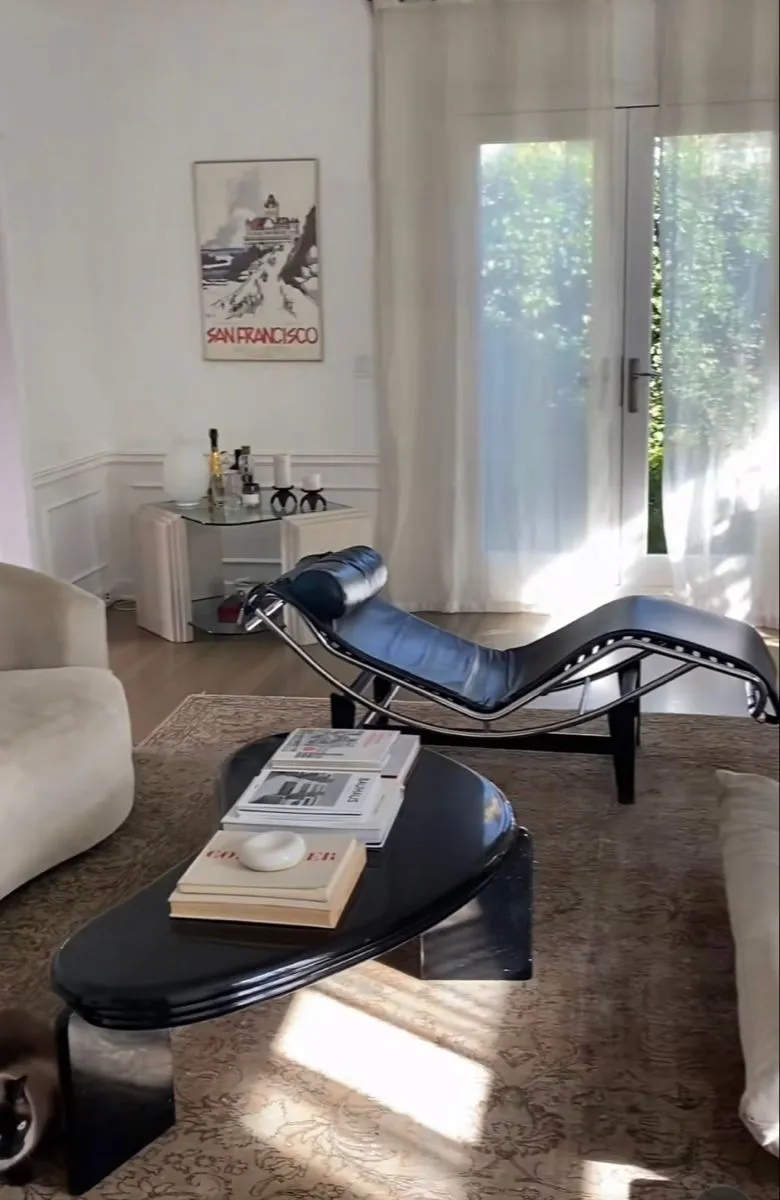 Black leather LC4 chaise longue in a sunlit living room with a sculptural coffee table
