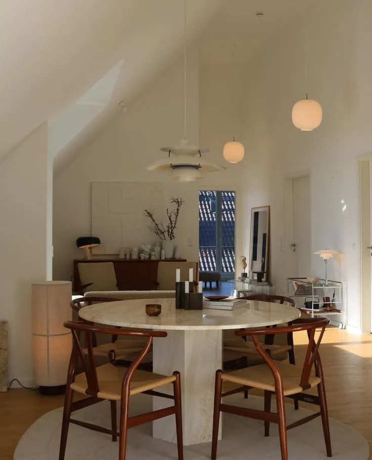 Wegner Wishbone Chairs around a round marble dining table under a sloped ceiling