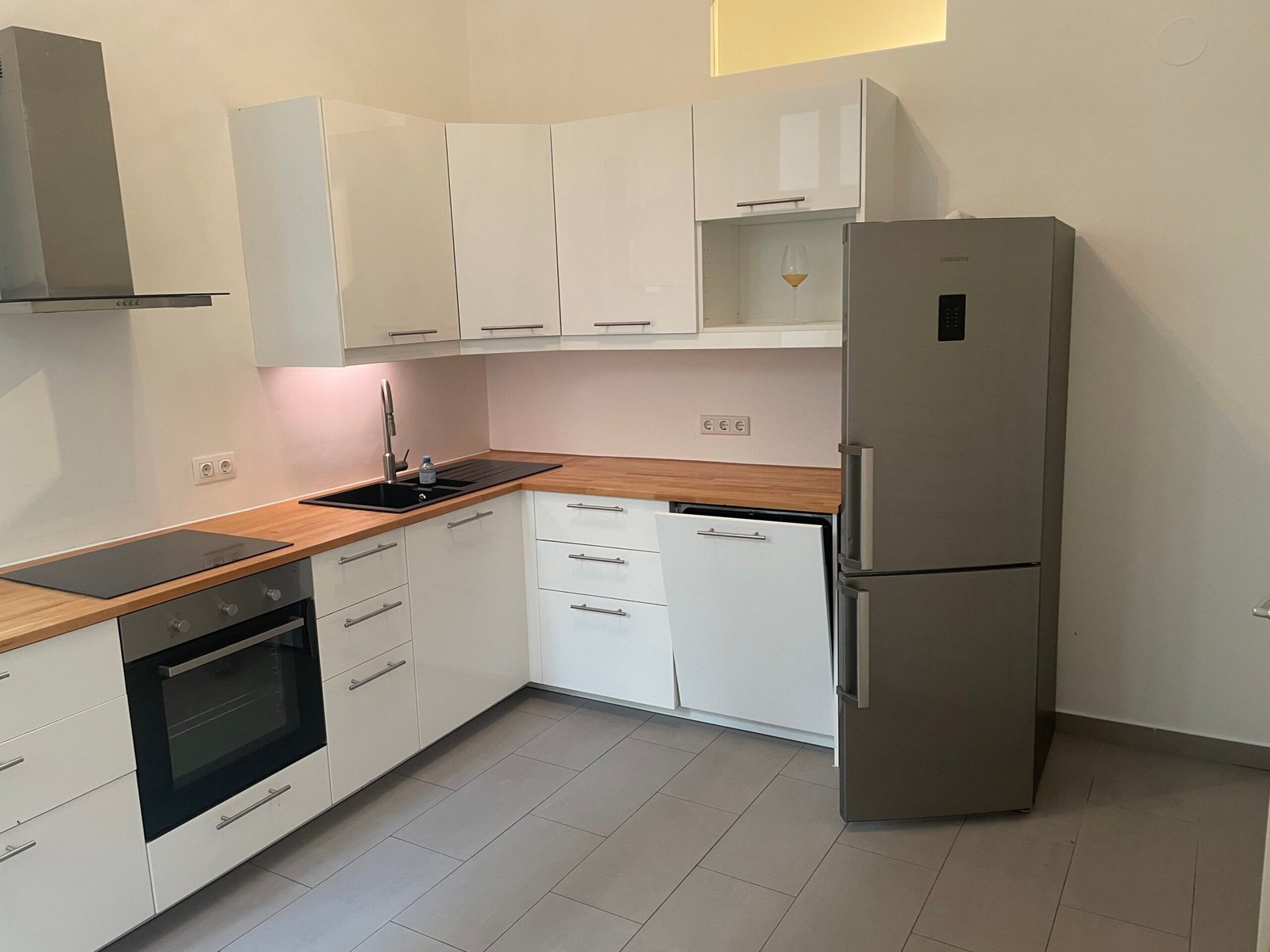 Before: plain white fitted kitchen with wooden worktops and a steel fridge