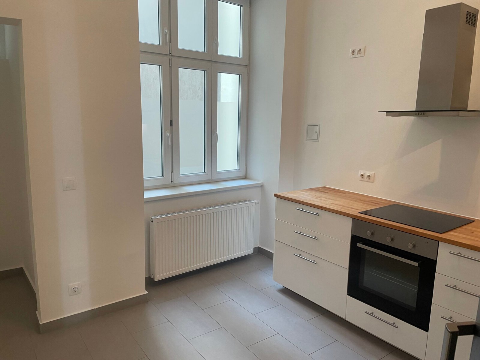 Before: empty kitchen with a tall window, radiator and white cabinets