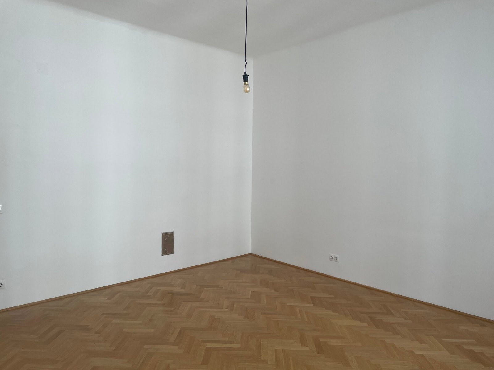 Before: empty white room corner with herringbone parquet and a bare bulb