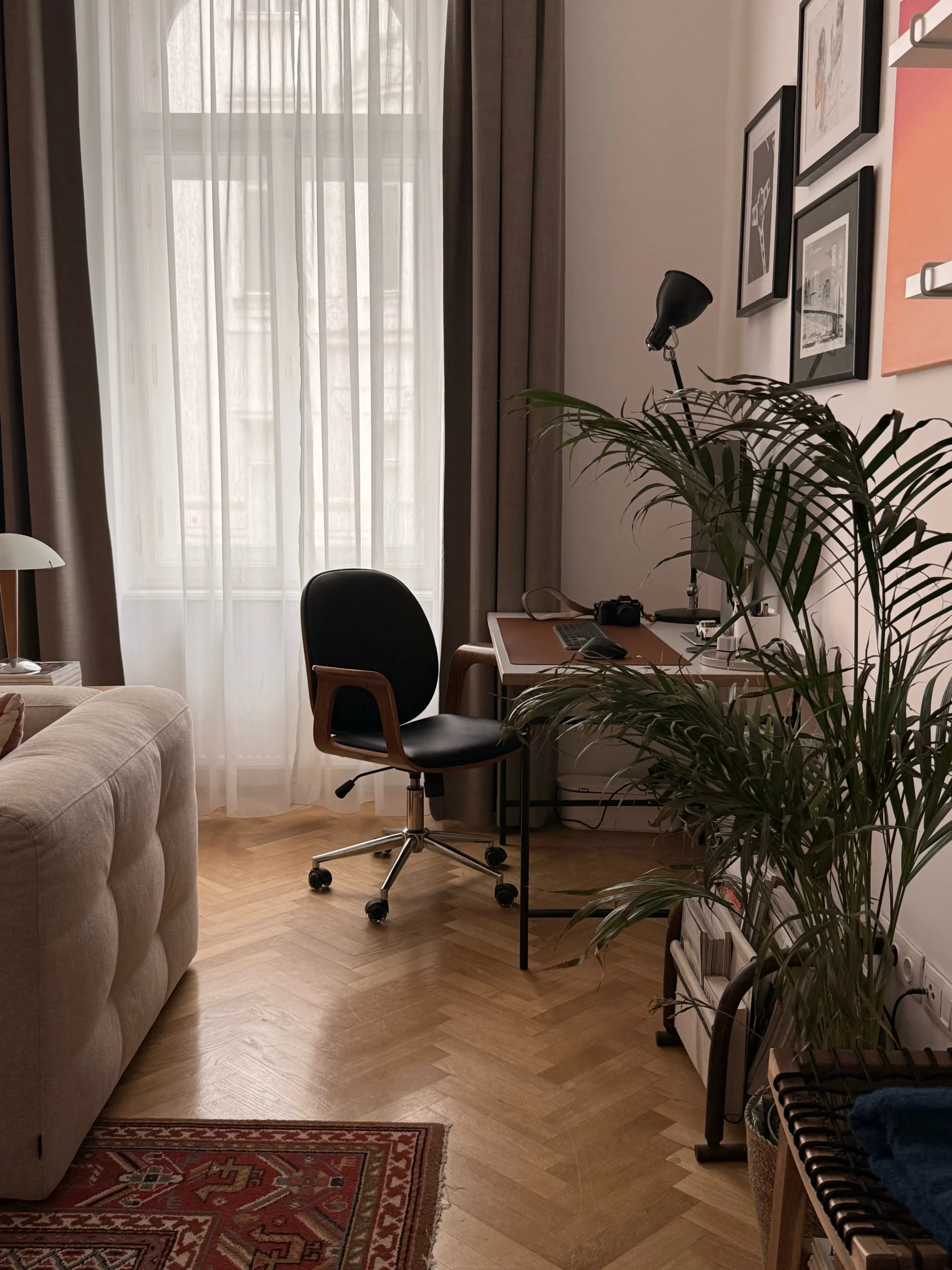 Home office corner with herringbone parquet, a vintage desk chair, a palm and a gallery wall by tall windows