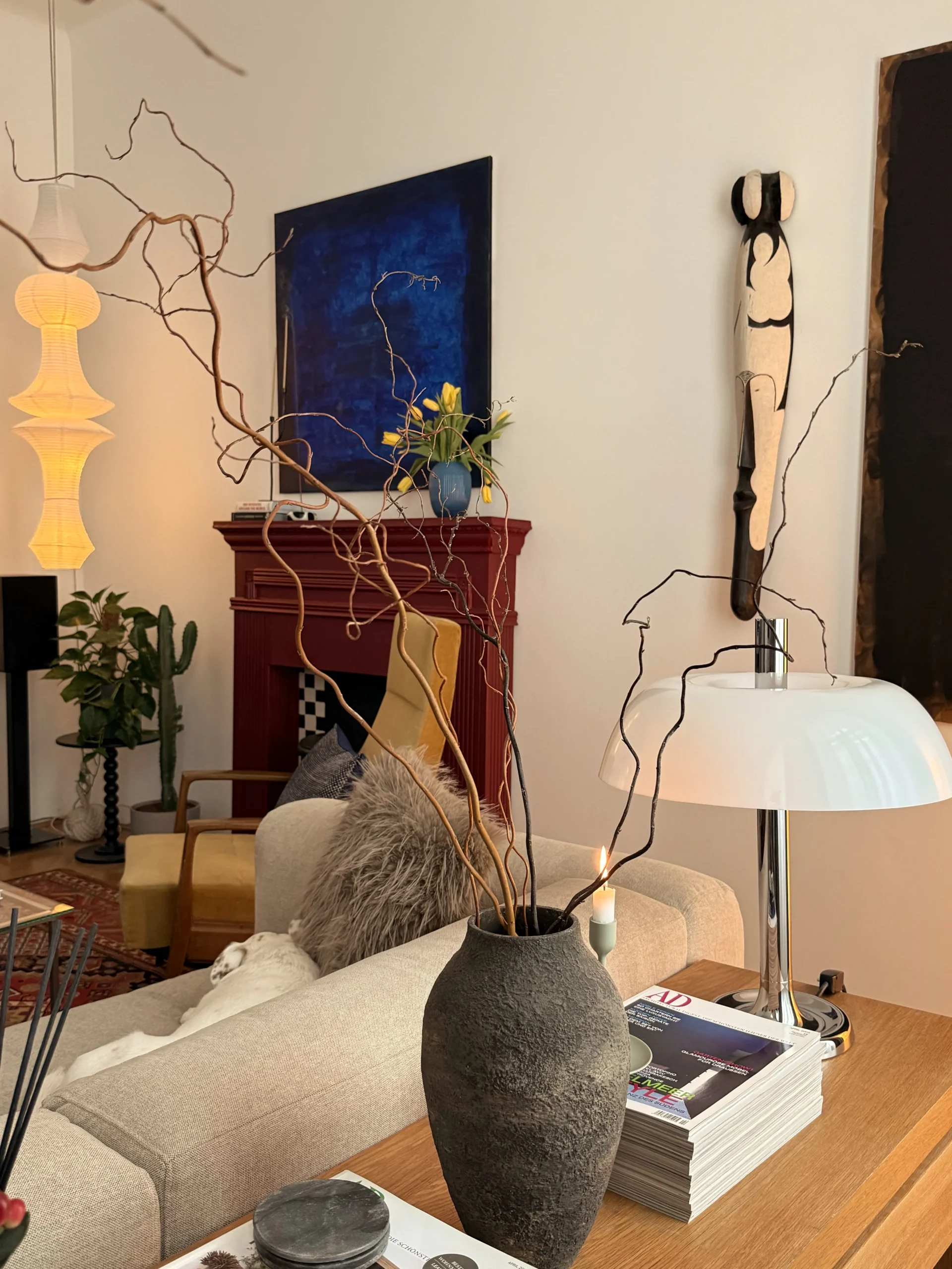 Living room with a red fireplace, blue painting, rice-paper floor lamp and white mushroom lamp, branches in a stone vase