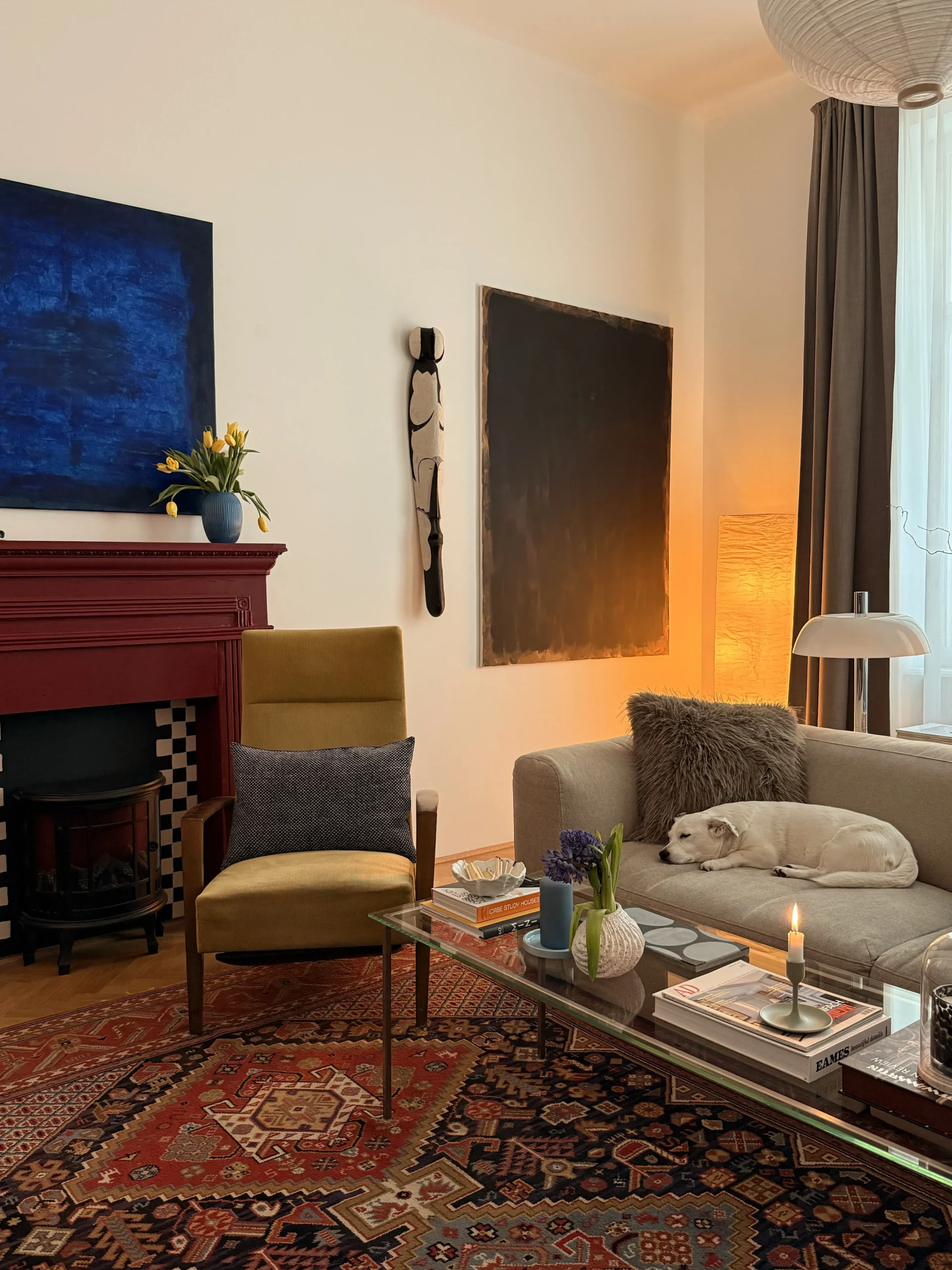 Living room with a red fireplace, mustard armchair, Persian rug, glass coffee table and a dog asleep on the sofa