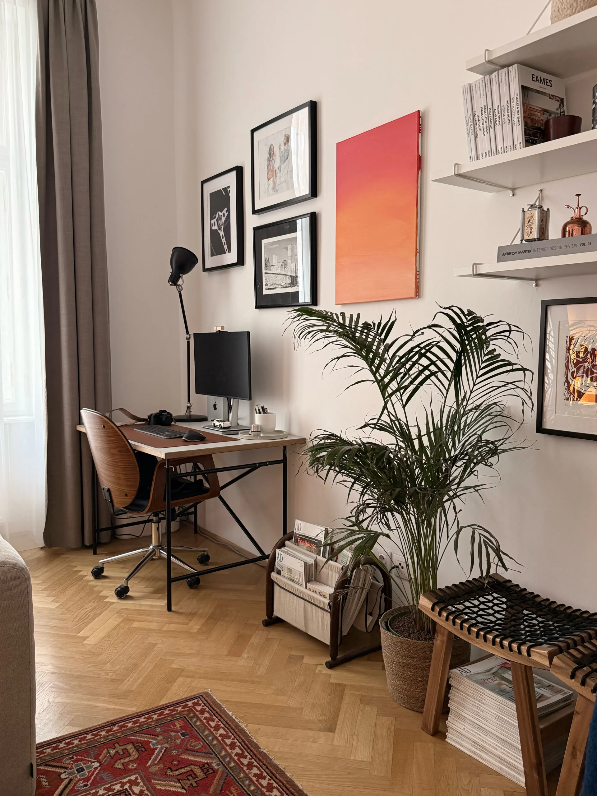 Home office with a gallery wall, orange-pink painting, palm and woven bench on herringbone parquet