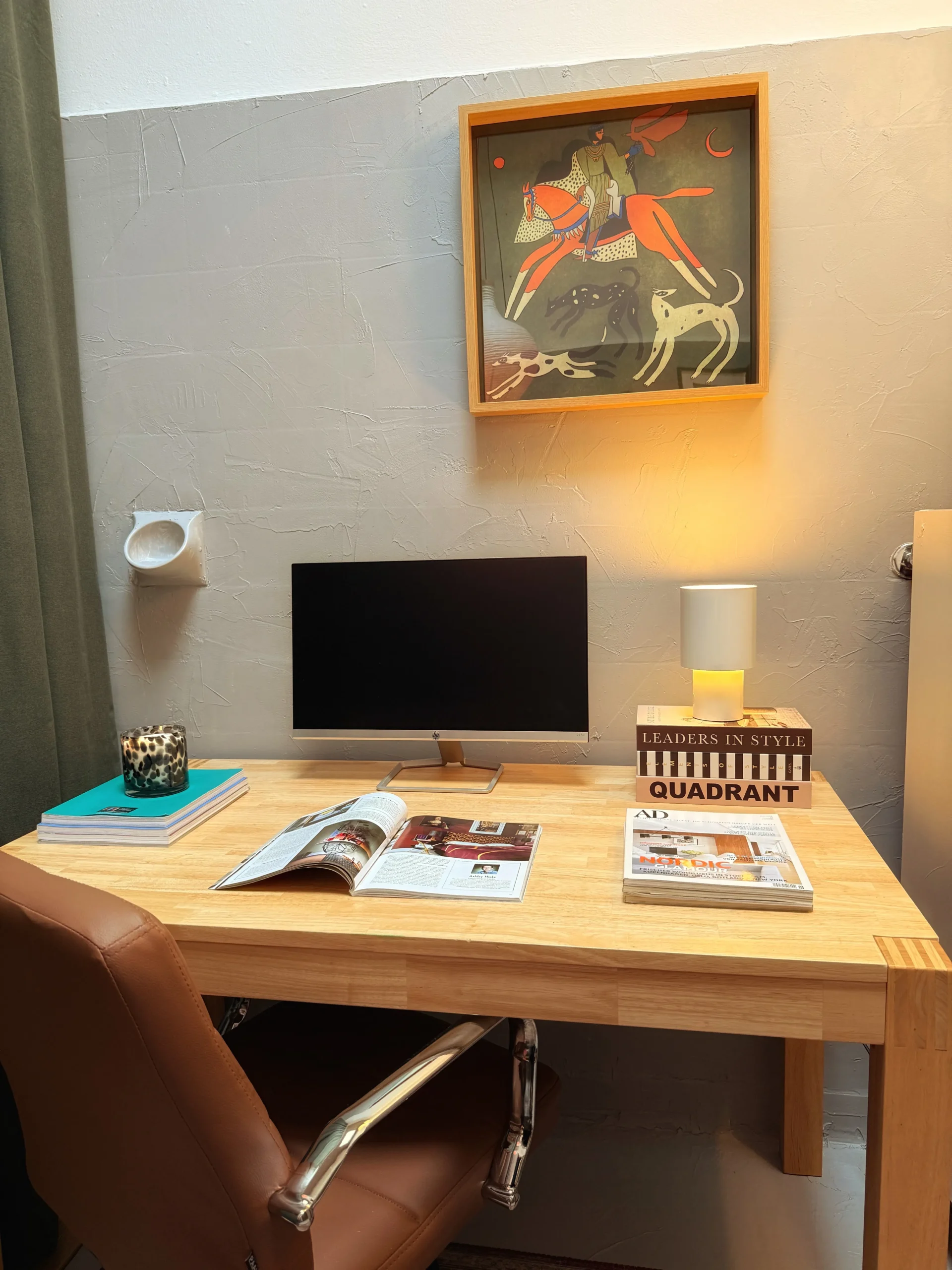 After: wooden desk with a monitor, design magazines and a framed painting in the converted office