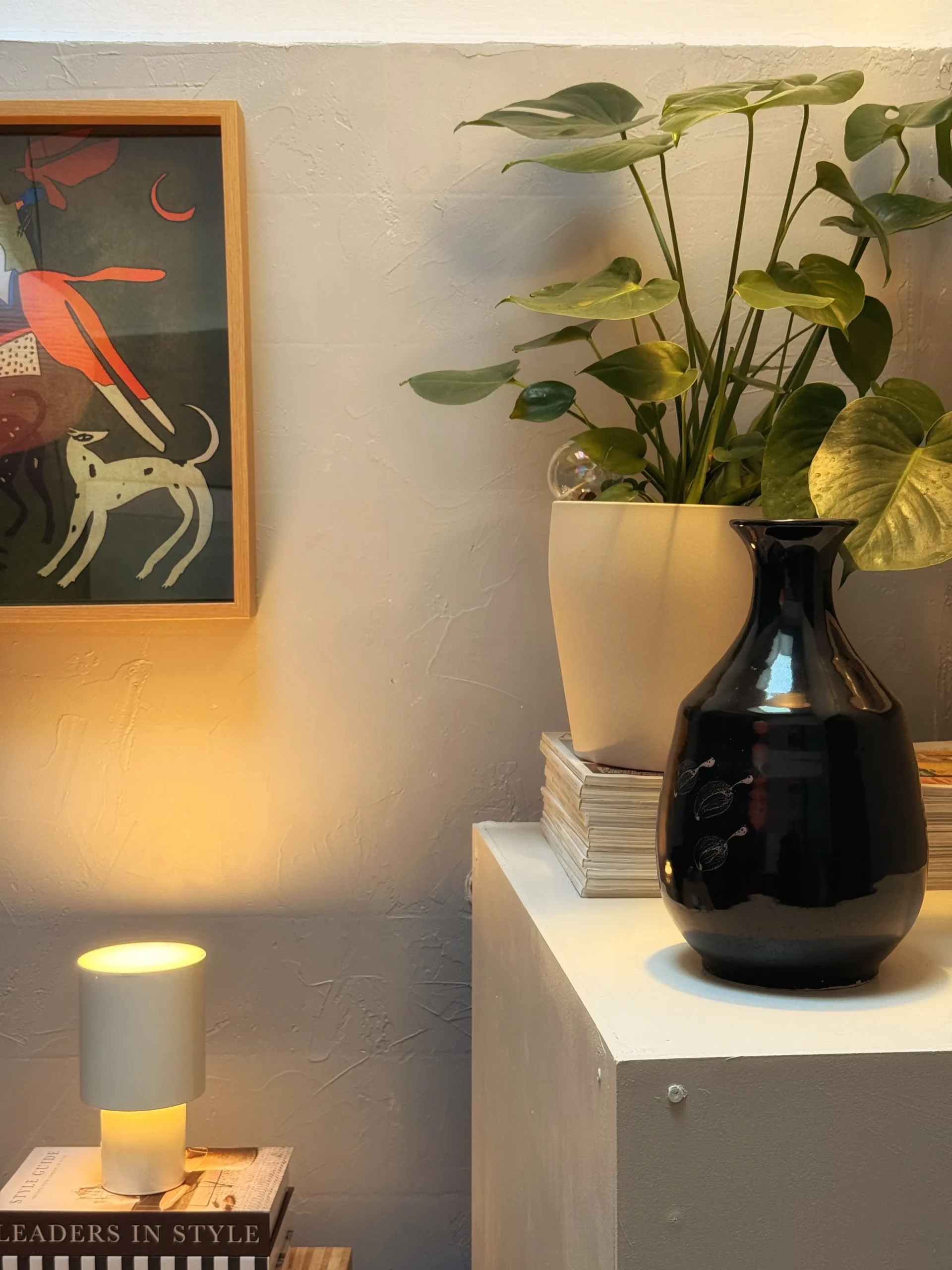 Black glass vase, monstera plant and a small table lamp on the white pedestal built over the old sink