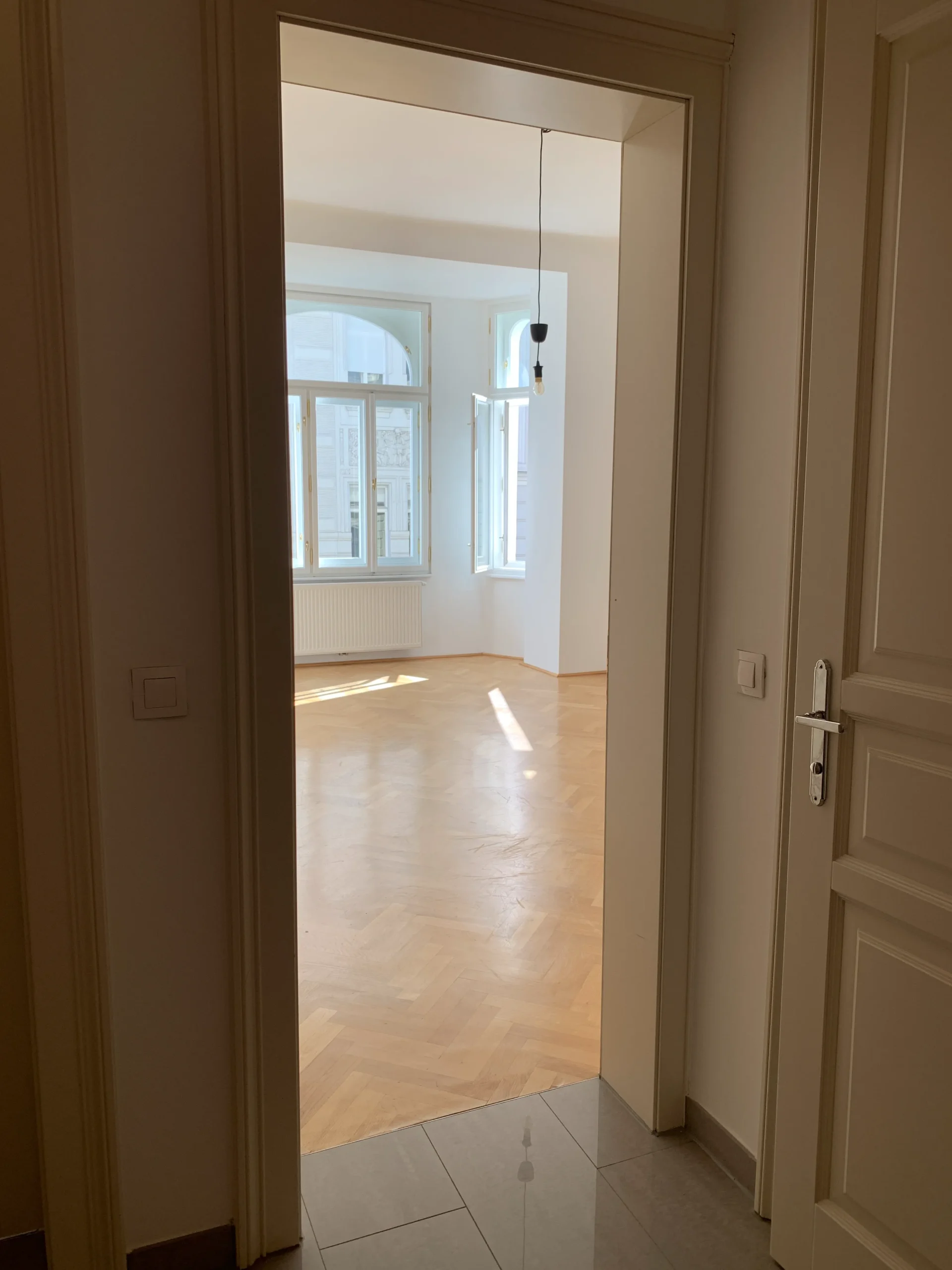 Before: view through a doorway into an empty room with a bay window and herringbone floor