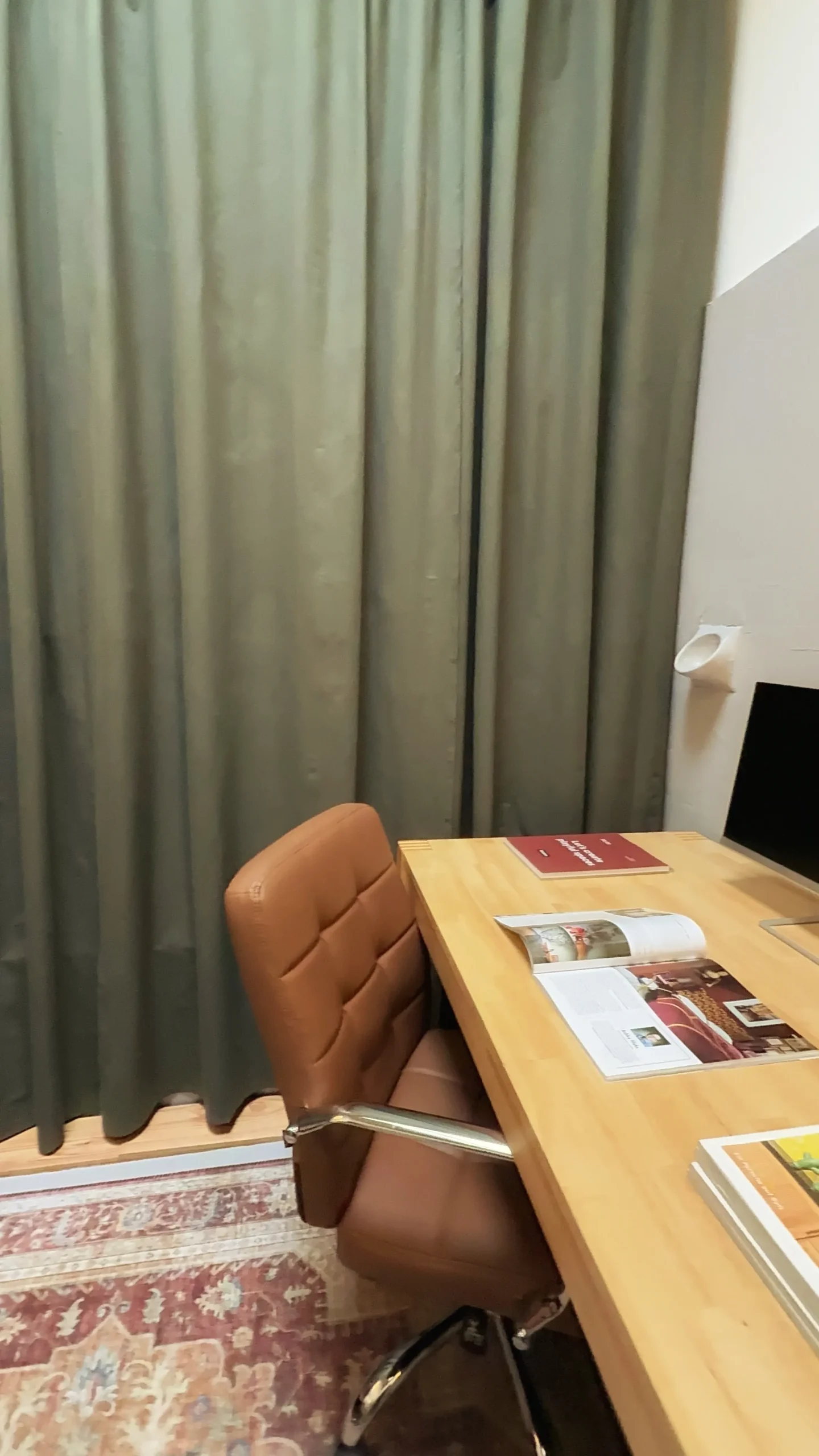 Leather desk chair at a wooden desk in front of a full-length green curtain