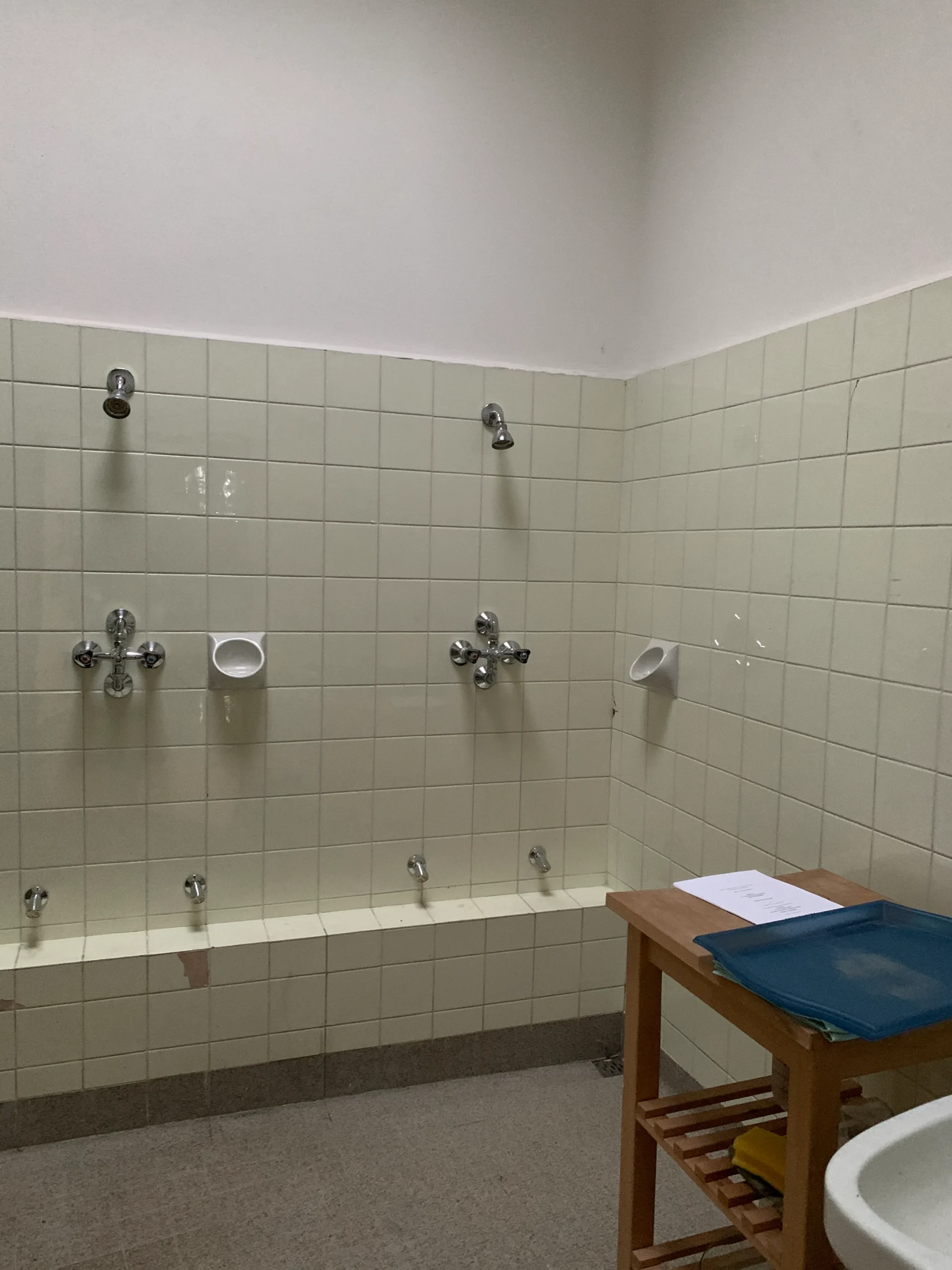 Before: tiled gym shower room in a former school, with exposed shower fittings and a wooden bench