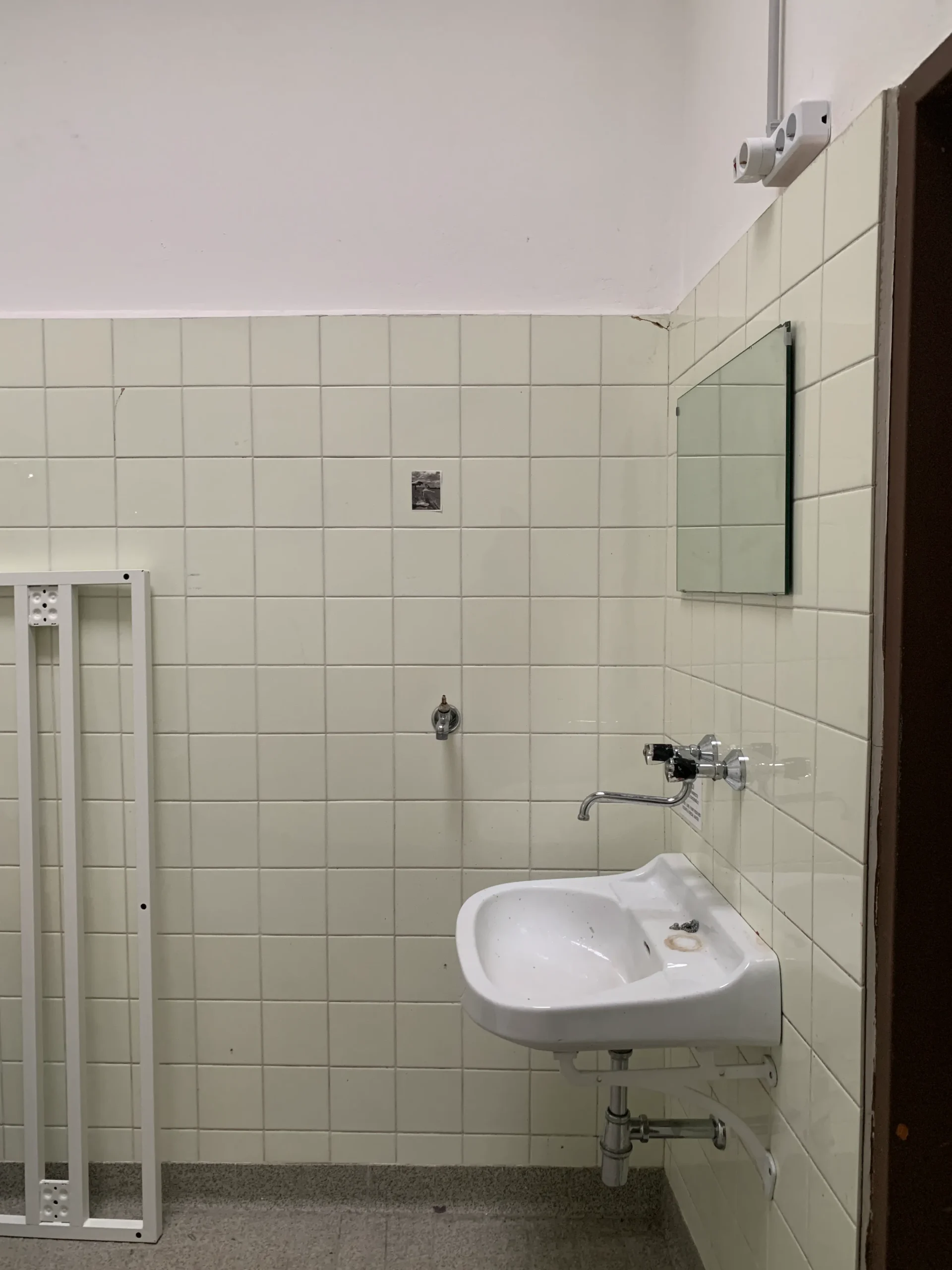 Before: tiled wall with a wall-mounted sink and mirror in the old shower room