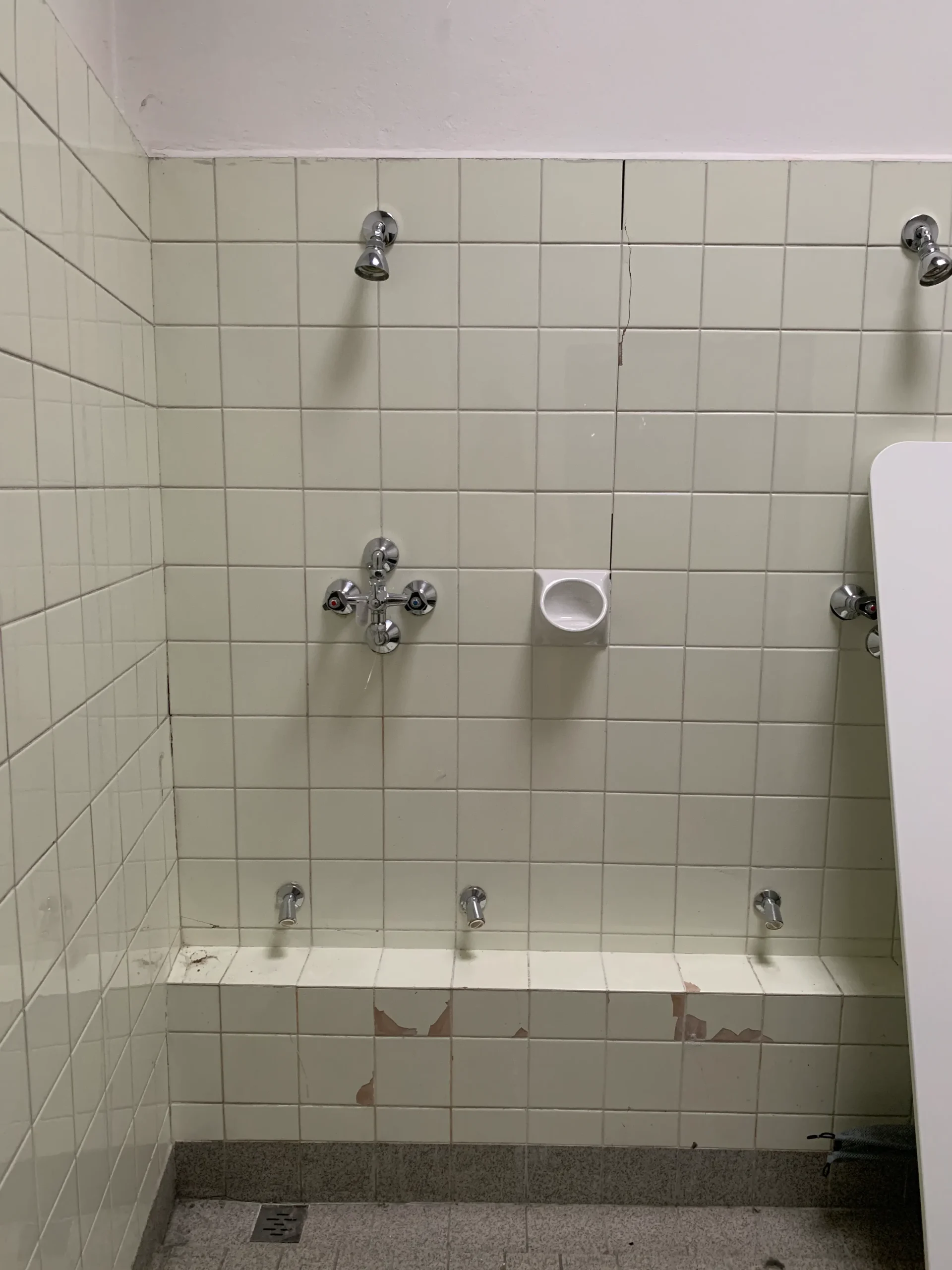 Before: row of shower fittings on a tiled wall in the old school shower room